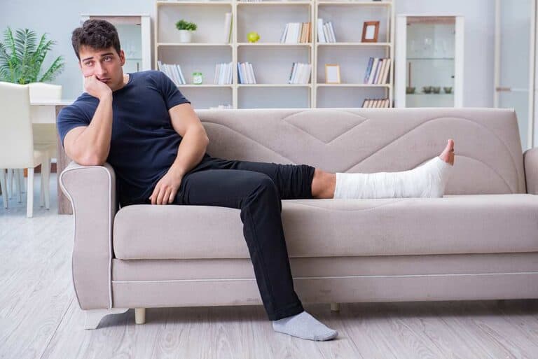 Man sitting on a couch with a cast on his leg waiting for his workers' comp settlement.