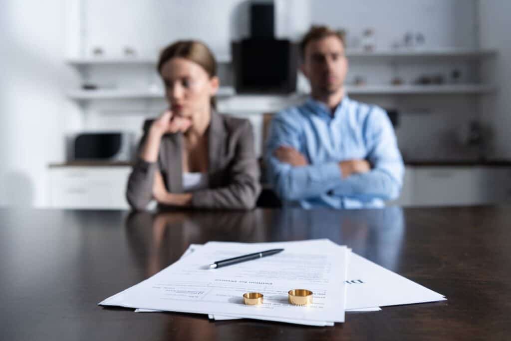 Picture of a couple going through a divorce trial while sitting at a table over divorce paperwork and wedding rings